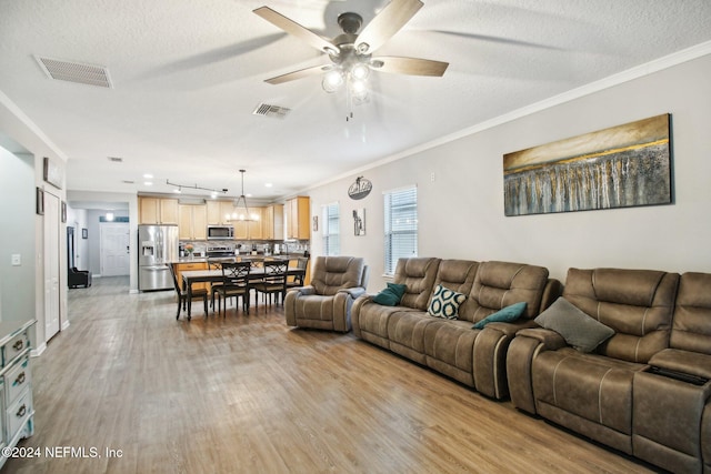 living room featuring a textured ceiling, ceiling fan, light wood-type flooring, and crown molding