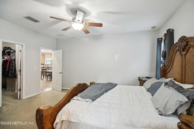 bedroom featuring a spacious closet, ceiling fan, light colored carpet, a textured ceiling, and a closet