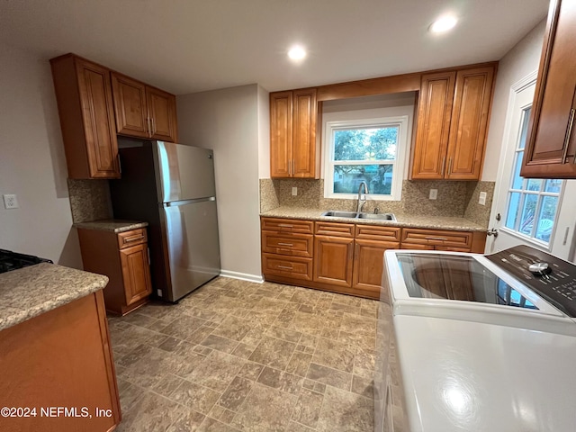 kitchen featuring white stove, sink, decorative backsplash, washer / dryer, and stainless steel refrigerator