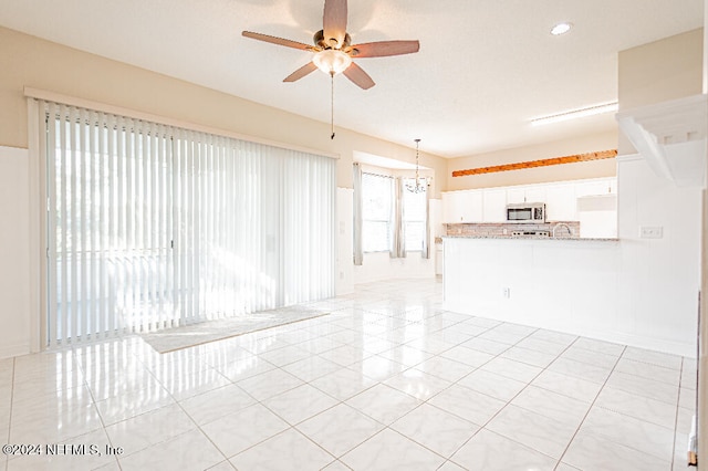 unfurnished living room featuring light tile patterned flooring and ceiling fan with notable chandelier