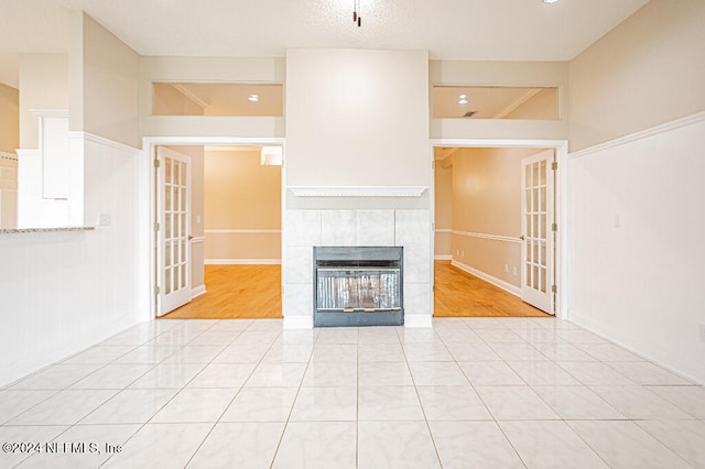 unfurnished living room with a tile fireplace, french doors, and light hardwood / wood-style floors