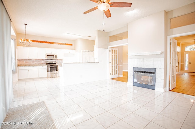 unfurnished living room with ceiling fan with notable chandelier, light tile patterned floors, a textured ceiling, and a tile fireplace