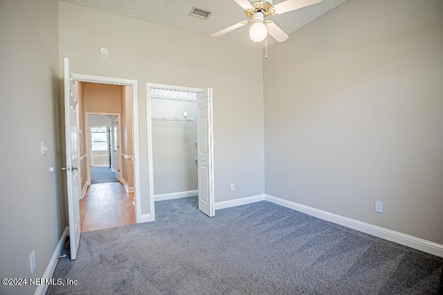 unfurnished bedroom with carpet, a textured ceiling, ceiling fan, a spacious closet, and a closet