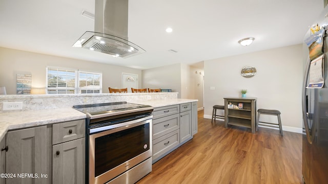 kitchen featuring gray cabinetry, island range hood, wood-type flooring, and stainless steel range with electric stovetop