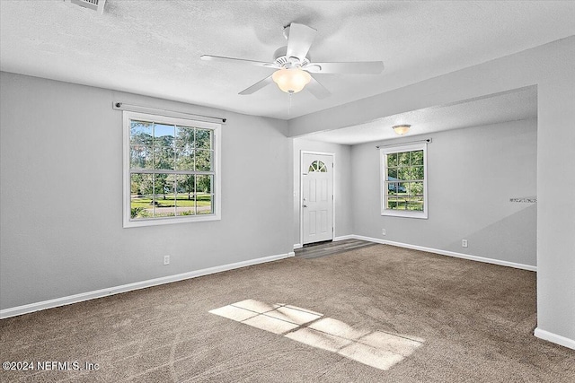 carpeted empty room featuring a textured ceiling, ceiling fan, and a healthy amount of sunlight