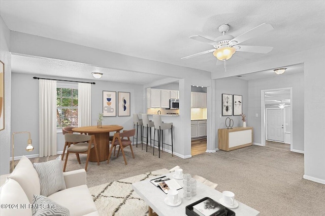 living room featuring ceiling fan, light colored carpet, and a textured ceiling