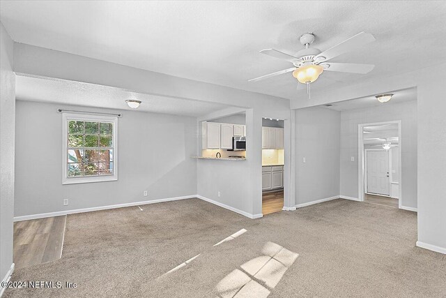 unfurnished living room with a textured ceiling, light colored carpet, and ceiling fan