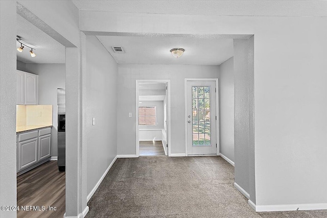 hall with a textured ceiling and dark colored carpet