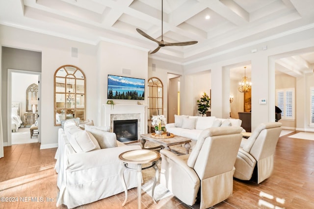 living room with coffered ceiling, light hardwood / wood-style flooring, a high end fireplace, ceiling fan with notable chandelier, and ornamental molding