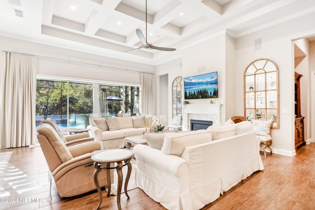 living room with coffered ceiling, ceiling fan, a towering ceiling, beamed ceiling, and light hardwood / wood-style floors