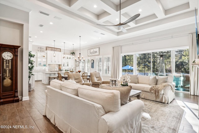 living room with dark hardwood / wood-style flooring, ornamental molding, coffered ceiling, ceiling fan with notable chandelier, and beamed ceiling