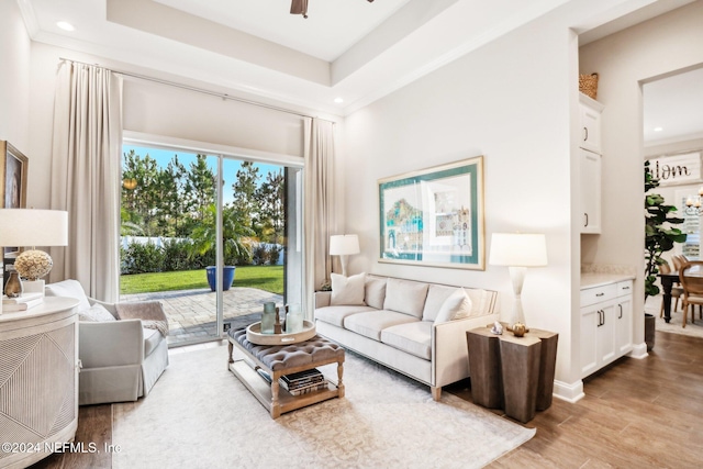 living room with a raised ceiling, ceiling fan, and light hardwood / wood-style flooring