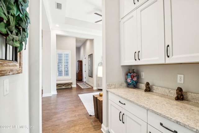 kitchen with light stone countertops, hardwood / wood-style floors, white cabinets, and ceiling fan