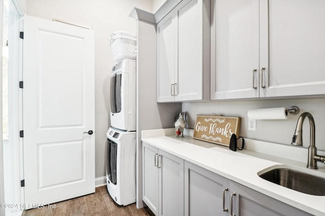 laundry room featuring cabinets, sink, stacked washing maching and dryer, and light hardwood / wood-style flooring