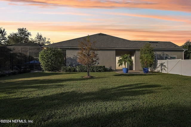 back house at dusk featuring a lawn and glass enclosure