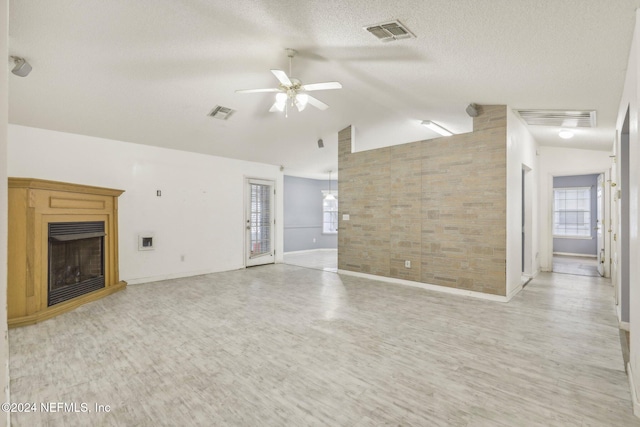 unfurnished living room with a textured ceiling, ceiling fan, light hardwood / wood-style flooring, and vaulted ceiling