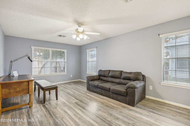 living room with ceiling fan, a textured ceiling, and light hardwood / wood-style flooring