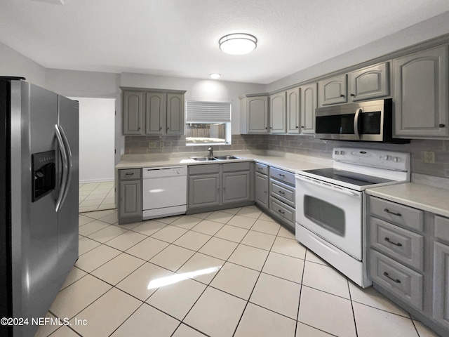 kitchen with gray cabinetry, backsplash, sink, and stainless steel appliances