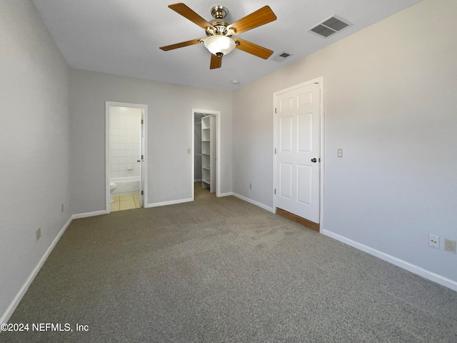 unfurnished bedroom with carpet floors, a spacious closet, ensuite bath, and ceiling fan