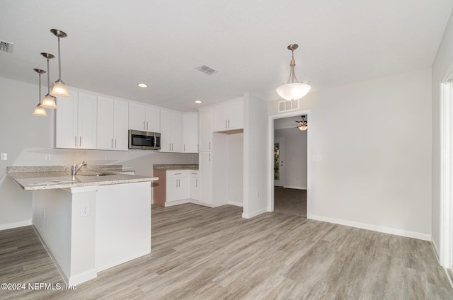 kitchen with kitchen peninsula, decorative light fixtures, white cabinetry, and light hardwood / wood-style floors