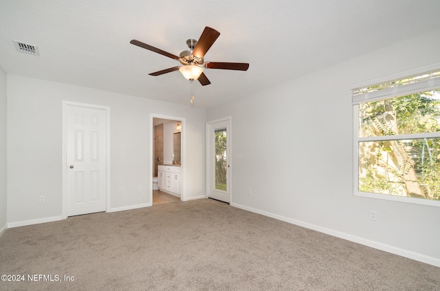 unfurnished bedroom featuring light carpet, connected bathroom, multiple windows, and ceiling fan