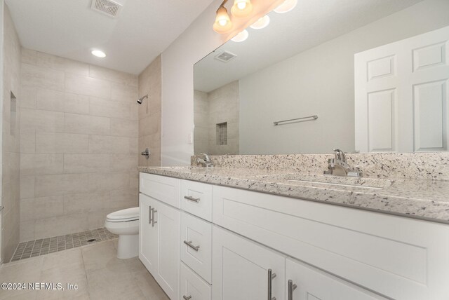 bathroom with a tile shower, tile patterned flooring, vanity, and toilet