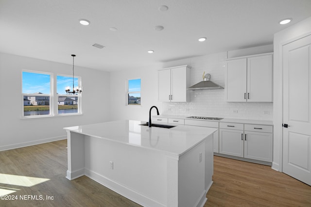 kitchen with a center island with sink, wall chimney exhaust hood, white cabinets, and sink