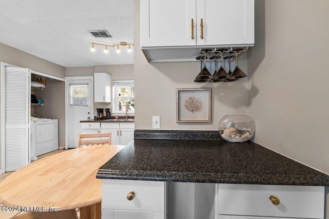 kitchen with dark stone counters, sink, a textured ceiling, white cabinetry, and washing machine and clothes dryer