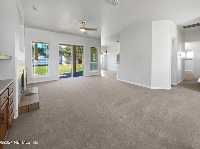 unfurnished living room featuring ceiling fan, light colored carpet, a textured ceiling, and a tiled fireplace