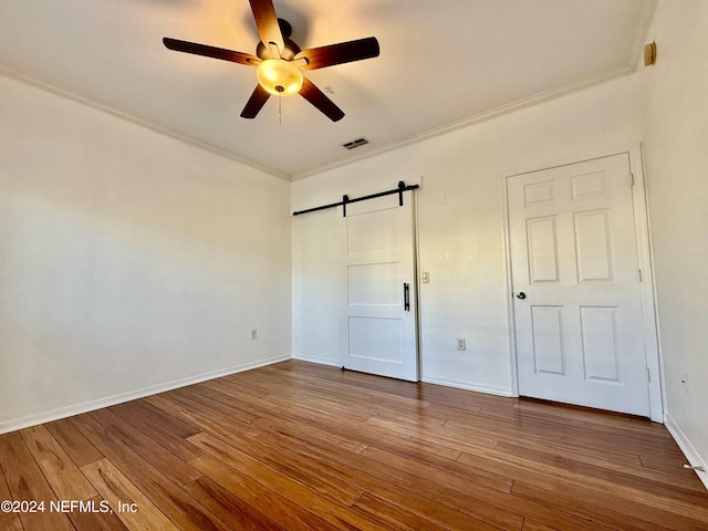 unfurnished bedroom featuring hardwood / wood-style floors, ceiling fan, a barn door, and ornamental molding