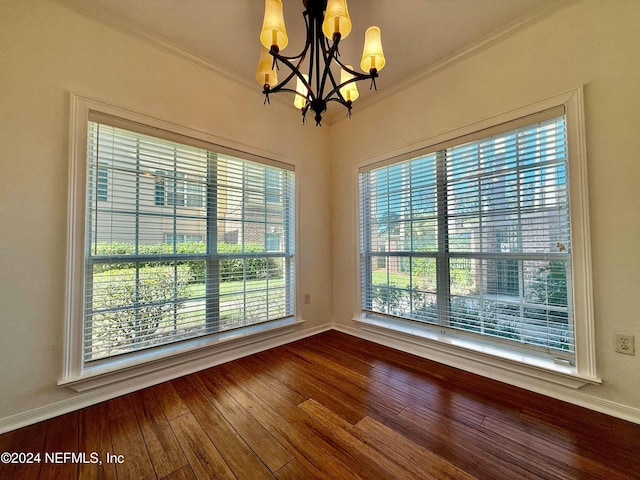 spare room with crown molding, plenty of natural light, wood-type flooring, and an inviting chandelier