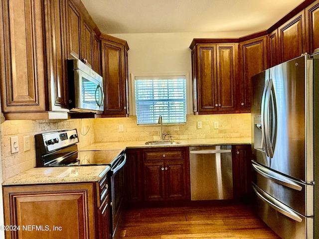 kitchen featuring dark hardwood / wood-style flooring, tasteful backsplash, light stone counters, stainless steel appliances, and sink