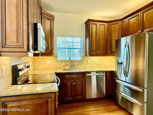 kitchen featuring sink, light stone countertops, appliances with stainless steel finishes, tasteful backsplash, and light hardwood / wood-style floors