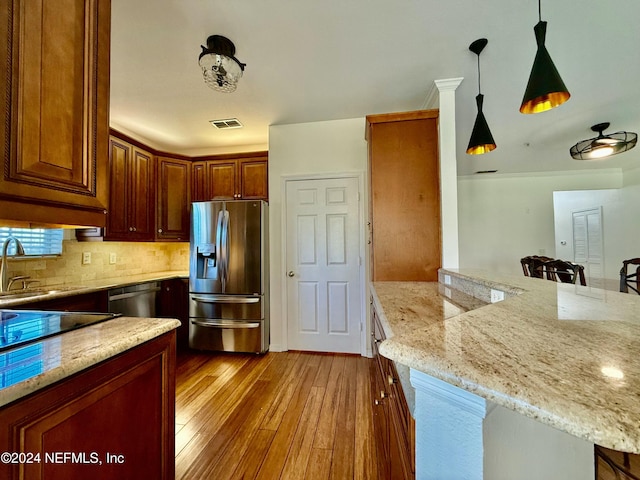 kitchen with light stone countertops, hanging light fixtures, stainless steel appliances, a kitchen breakfast bar, and light hardwood / wood-style flooring