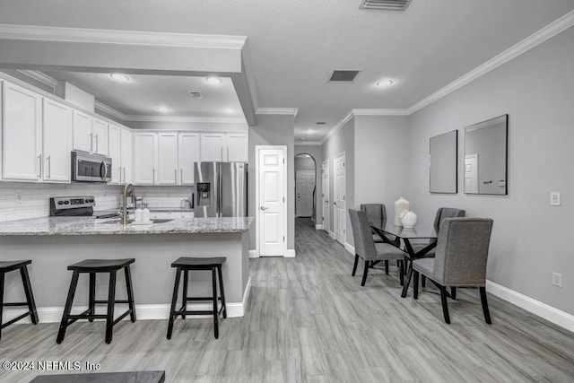 kitchen featuring white cabinetry, stainless steel appliances, kitchen peninsula, a kitchen bar, and ornamental molding