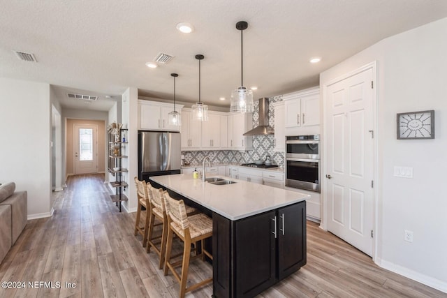 kitchen with appliances with stainless steel finishes, sink, a center island with sink, light hardwood / wood-style floors, and white cabinetry