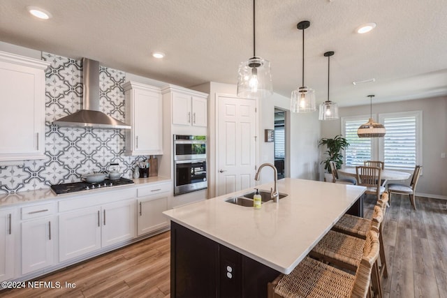 kitchen featuring white cabinetry, sink, wall chimney range hood, black gas cooktop, and pendant lighting