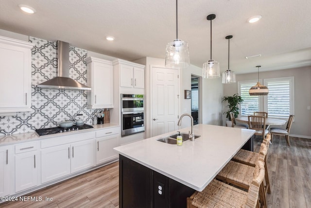 kitchen with pendant lighting, a kitchen island with sink, black gas cooktop, wall chimney range hood, and sink