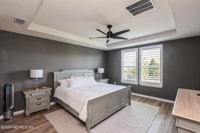 bedroom featuring wood-type flooring, a textured ceiling, a tray ceiling, and ceiling fan