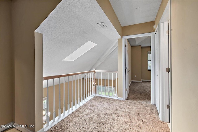 hallway with a textured ceiling, light colored carpet, and a healthy amount of sunlight