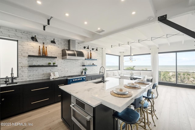 1304 Strand St, Neptune Beach, FL 32266 - kitchen featuring dark cabinets, wall chimney exhaust hood, open shelves, a sink, and beam ceiling