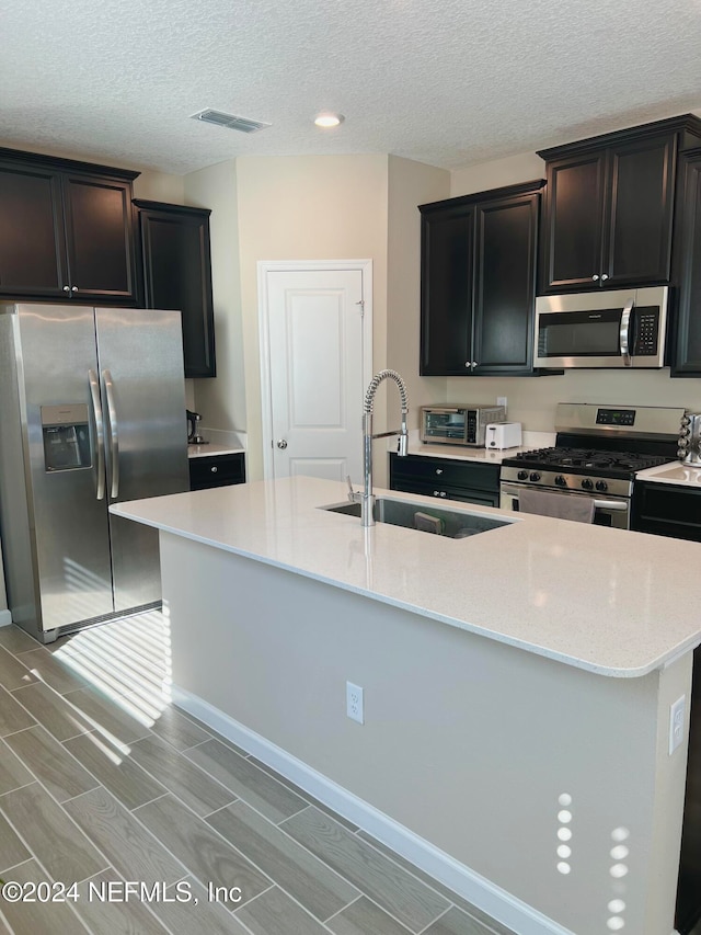 kitchen featuring sink, an island with sink, light hardwood / wood-style floors, and appliances with stainless steel finishes