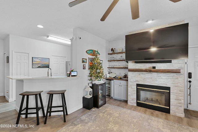 kitchen featuring kitchen peninsula, a kitchen bar, light hardwood / wood-style flooring, wine cooler, and a stone fireplace