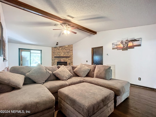 living room with ceiling fan, dark wood-type flooring, a stone fireplace, lofted ceiling with beams, and a textured ceiling