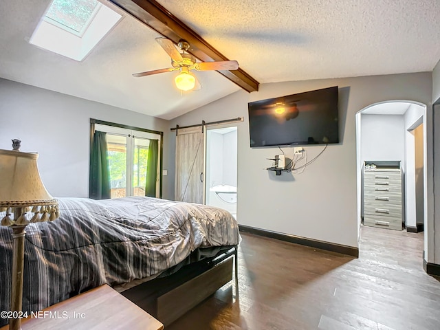 bedroom featuring ensuite bath, lofted ceiling with skylight, ceiling fan, wood-type flooring, and a barn door