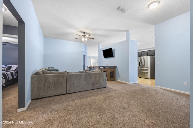 living room with a textured ceiling, carpet floors, and ceiling fan