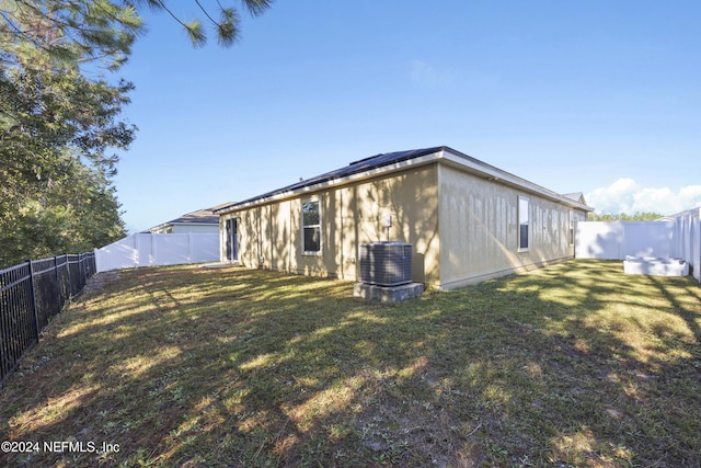 rear view of house featuring cooling unit and a lawn