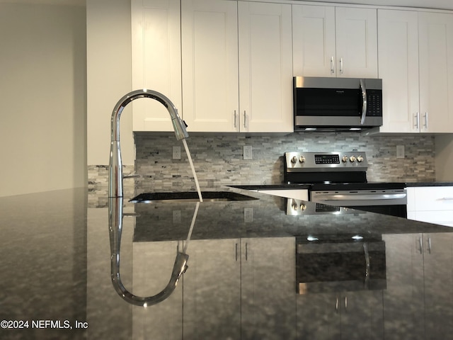 kitchen featuring sink, white cabinetry, backsplash, dark stone countertops, and stainless steel appliances