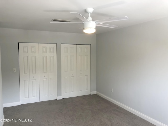 unfurnished bedroom featuring multiple closets, ceiling fan, and dark carpet