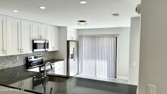 kitchen with appliances with stainless steel finishes, white cabinetry, sink, backsplash, and dark stone counters